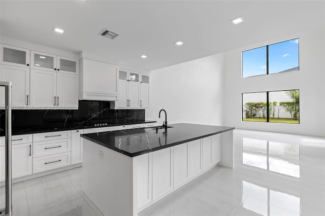 kitchen featuring visible vents, a sink, glass insert cabinets, white cabinets, and decorative backsplash