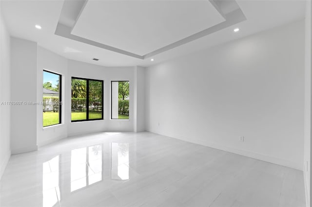 empty room featuring a raised ceiling, recessed lighting, baseboards, and visible vents