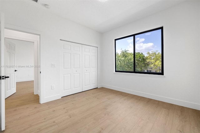 unfurnished bedroom featuring light wood-style floors, baseboards, and a closet