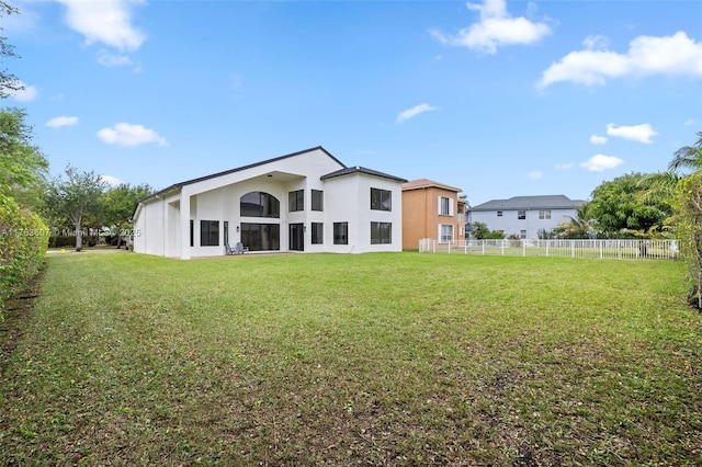 rear view of property with fence, a lawn, and stucco siding