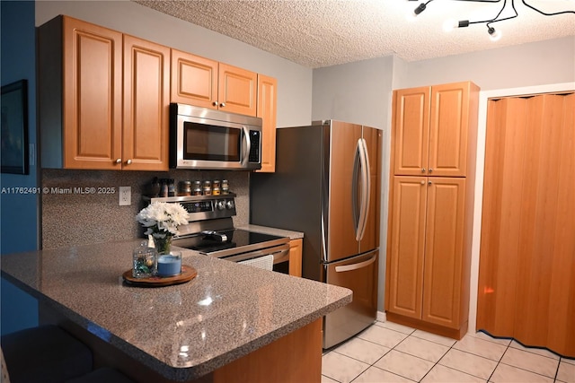 kitchen with light tile patterned floors, a peninsula, stainless steel appliances, a textured ceiling, and backsplash