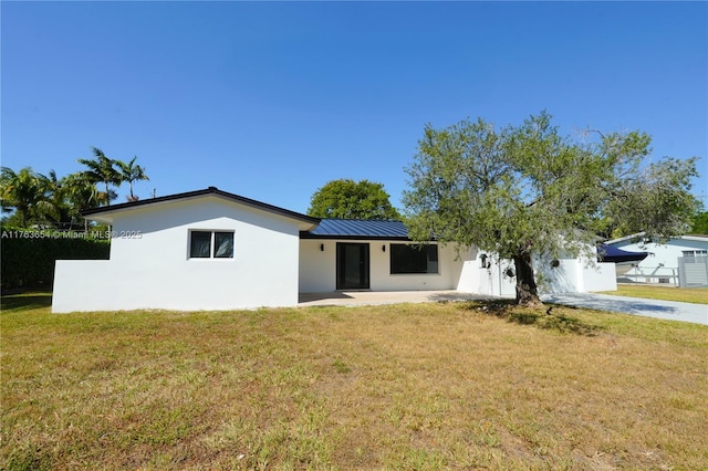 ranch-style house featuring stucco siding, driveway, a standing seam roof, a front yard, and metal roof