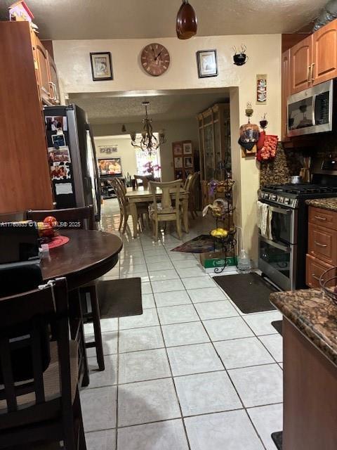 kitchen featuring dark stone counters, light tile patterned flooring, stainless steel appliances, pendant lighting, and a notable chandelier