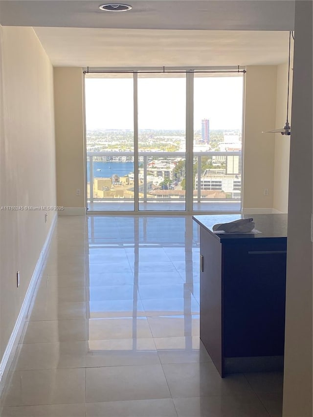 spare room featuring a wall of windows, baseboards, and light tile patterned floors