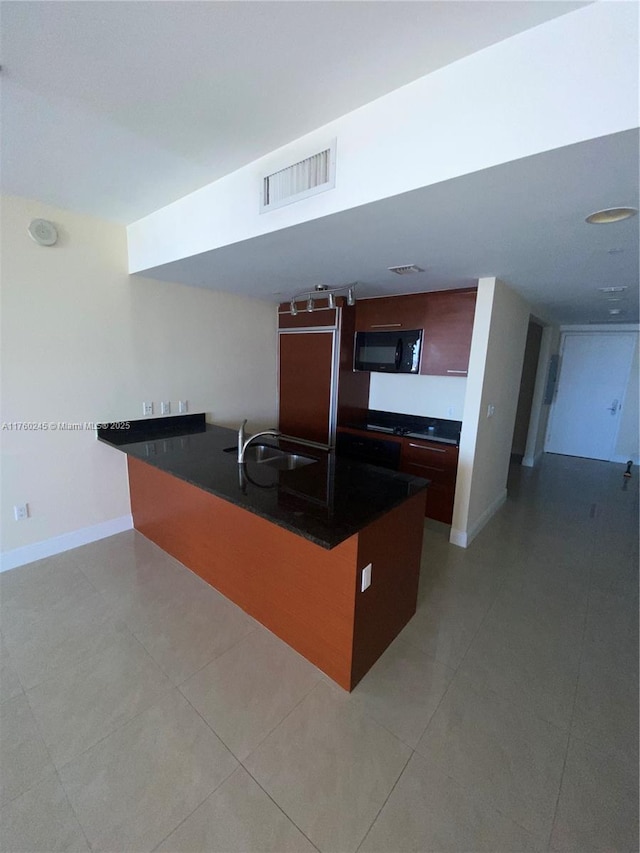 kitchen with dark countertops, visible vents, black microwave, a peninsula, and a sink