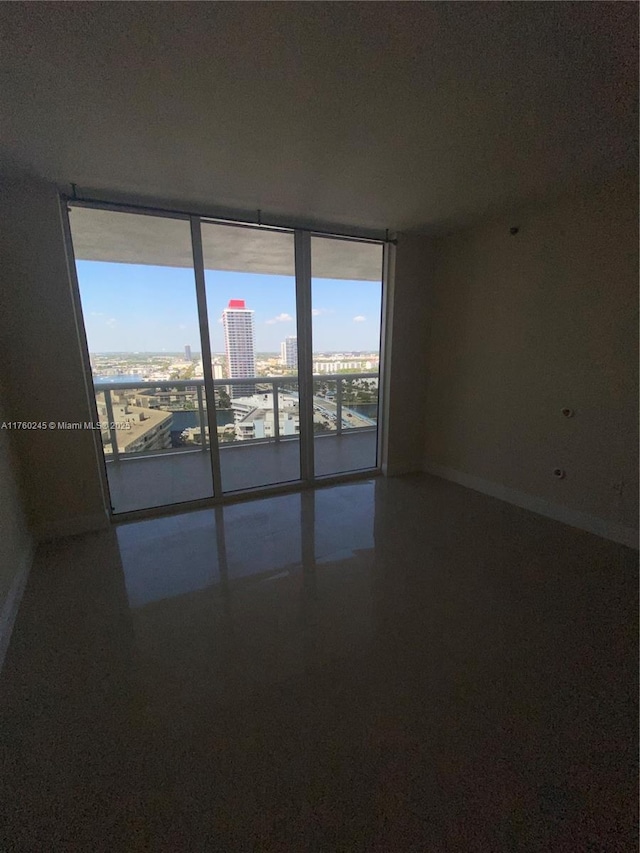 spare room featuring a city view, floor to ceiling windows, speckled floor, and baseboards