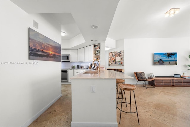 kitchen with a breakfast bar area, open shelves, a sink, stainless steel appliances, and white cabinets