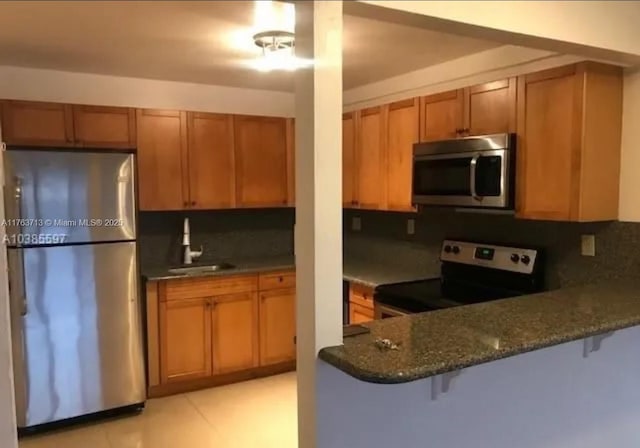 kitchen with a sink, dark stone counters, backsplash, and stainless steel appliances