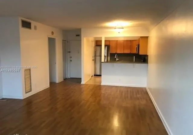 kitchen featuring brown cabinets, wood finished floors, freestanding refrigerator, a peninsula, and baseboards