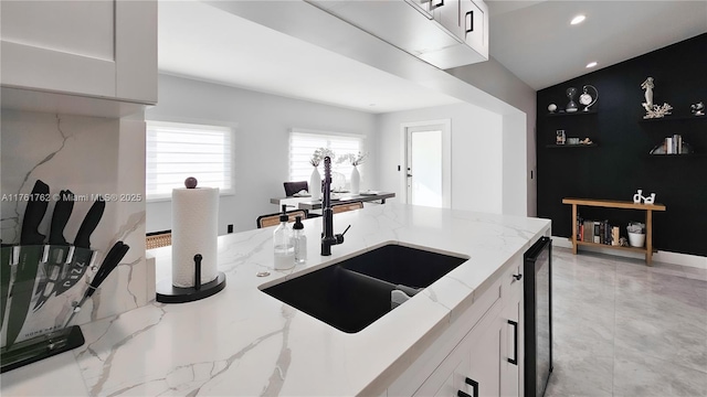 kitchen featuring a sink, light stone countertops, beverage cooler, and white cabinetry