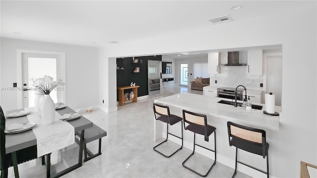 kitchen featuring visible vents, a sink, a kitchen breakfast bar, white cabinetry, and wall chimney exhaust hood