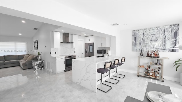 kitchen featuring a sink, appliances with stainless steel finishes, a breakfast bar area, white cabinets, and wall chimney range hood