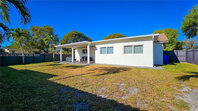 rear view of property featuring stucco siding, a lawn, a fenced backyard, and a patio area