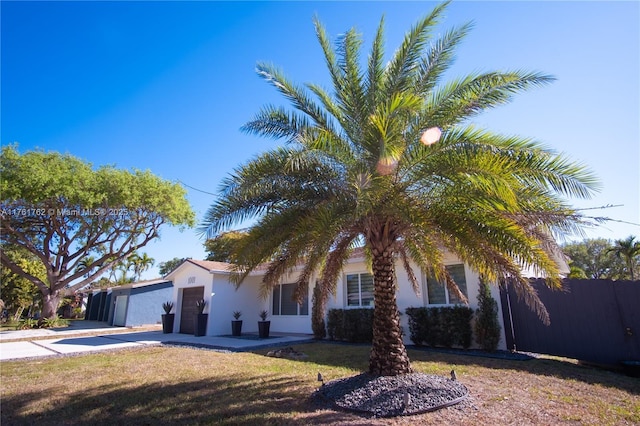 view of front facade with a front yard, fence, driveway, stucco siding, and a garage