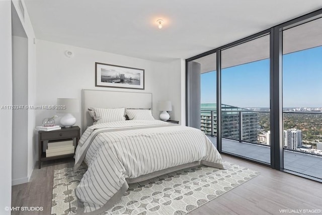 bedroom with access to outside, wood finished floors, baseboards, expansive windows, and a view of city