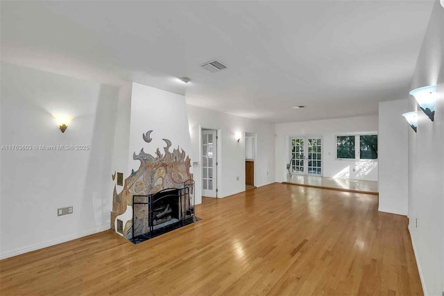 unfurnished living room featuring light wood-type flooring, visible vents, french doors, a stone fireplace, and baseboards