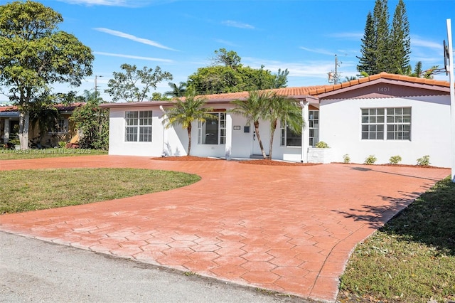 ranch-style home with curved driveway, a tiled roof, a front lawn, and stucco siding