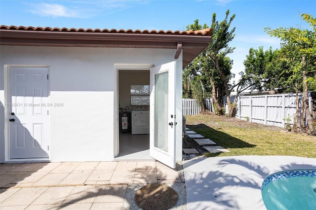 exterior space with fence, a tile roof, washer / dryer, stucco siding, and a yard