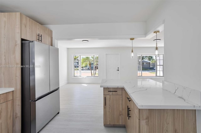 kitchen featuring light brown cabinetry, light stone counters, decorative light fixtures, freestanding refrigerator, and light wood finished floors