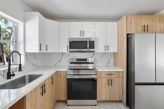 kitchen with light stone counters, a sink, appliances with stainless steel finishes, white cabinetry, and backsplash