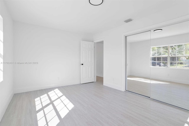 unfurnished bedroom featuring a closet, visible vents, baseboards, and wood finished floors