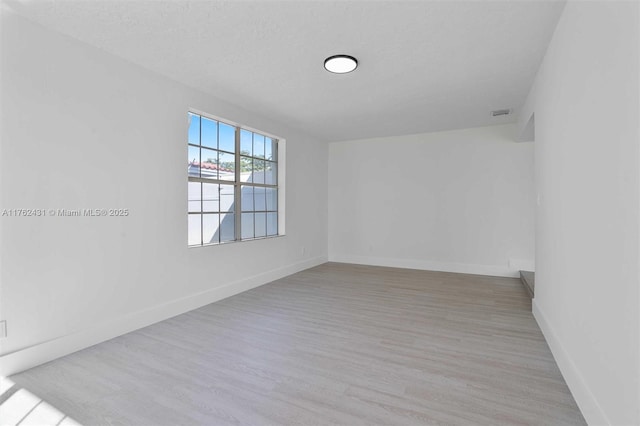 spare room featuring baseboards, a textured ceiling, and wood finished floors