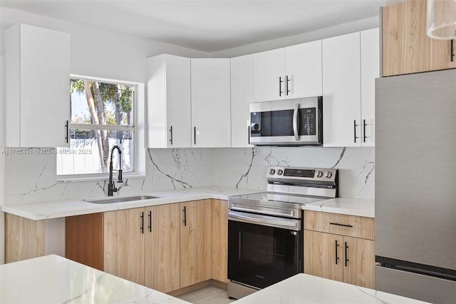 kitchen featuring a sink, backsplash, appliances with stainless steel finishes, white cabinets, and light stone countertops