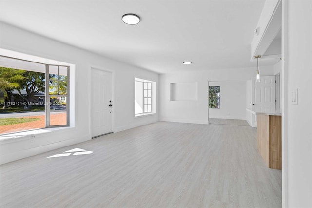 unfurnished living room featuring baseboards, plenty of natural light, and light wood-style flooring