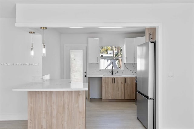 kitchen with a peninsula, freestanding refrigerator, a sink, light wood-type flooring, and backsplash