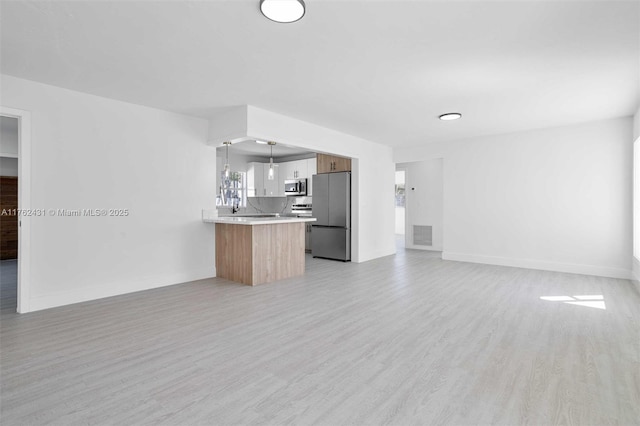 kitchen with open floor plan, light countertops, light wood-style flooring, appliances with stainless steel finishes, and a peninsula