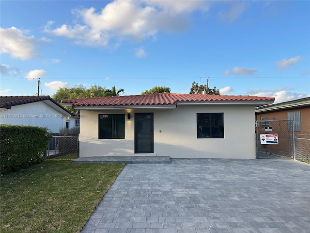 view of front facade with stucco siding, a tile roof, a front yard, and fence