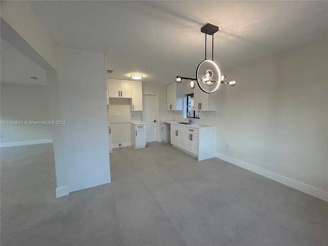 kitchen with baseboards, white cabinets, a sink, and a chandelier