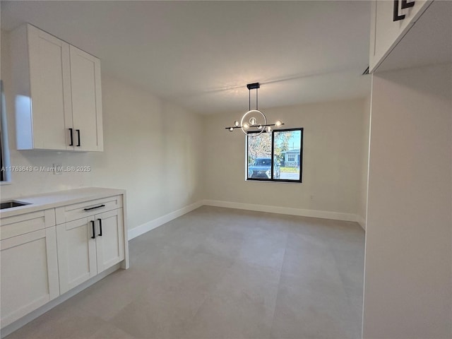 unfurnished dining area featuring an inviting chandelier, a sink, and baseboards