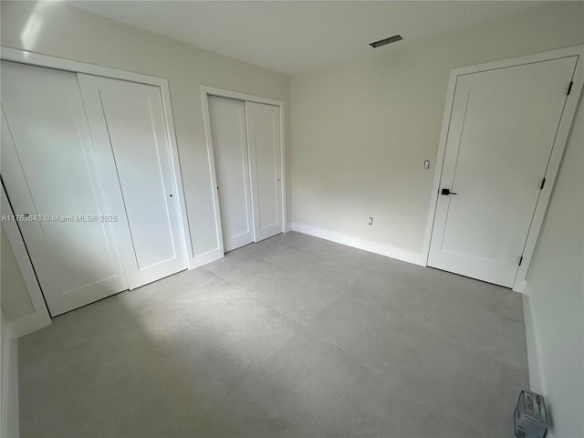 unfurnished bedroom with baseboards, visible vents, and two closets