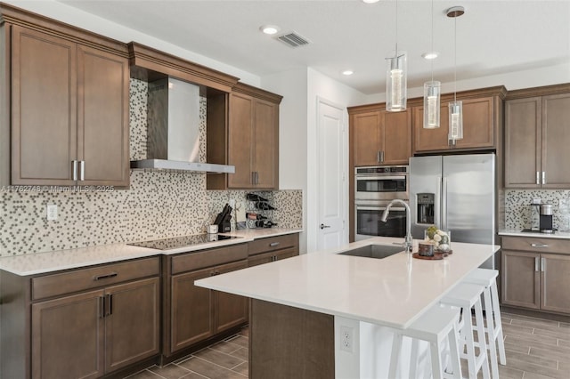 kitchen with wood finish floors, stainless steel appliances, decorative backsplash, a sink, and wall chimney range hood