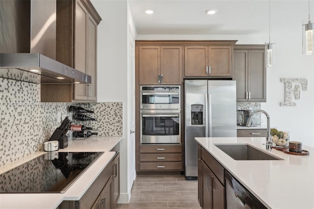 kitchen with tasteful backsplash, wall chimney exhaust hood, stainless steel appliances, and a sink