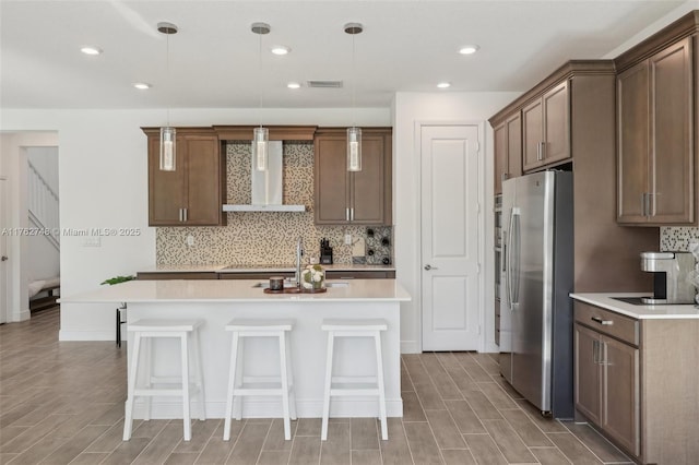 kitchen with visible vents, wall chimney range hood, stainless steel fridge with ice dispenser, a kitchen bar, and light countertops