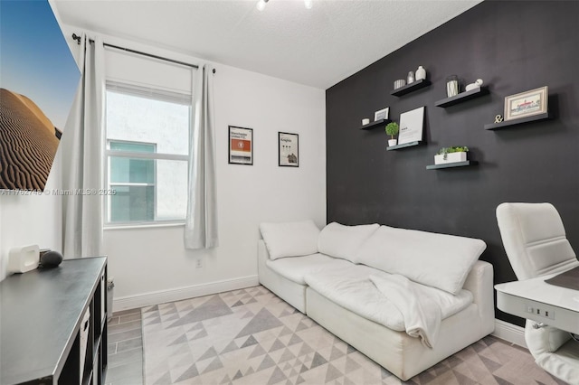 living area featuring an accent wall, light floors, baseboards, and a textured ceiling