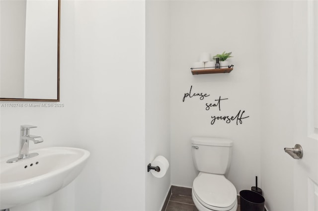 half bathroom featuring tile patterned floors, toilet, baseboards, and a sink