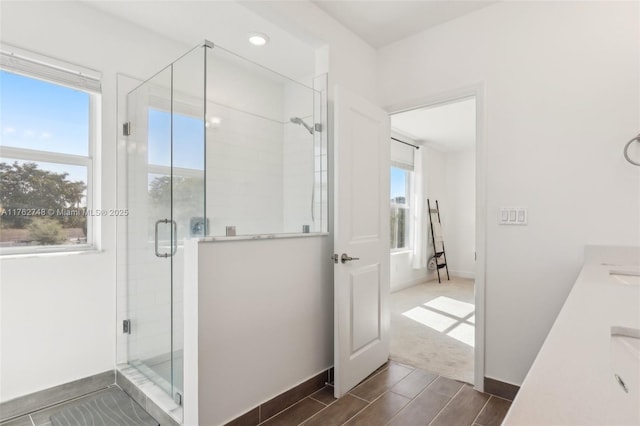 full bath featuring wood tiled floor, a shower stall, baseboards, and double vanity