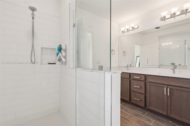 bathroom featuring visible vents, walk in shower, wood tiled floor, double vanity, and a sink