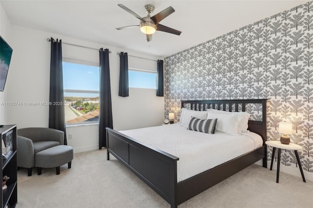 bedroom featuring light carpet, wallpapered walls, baseboards, ceiling fan, and an accent wall