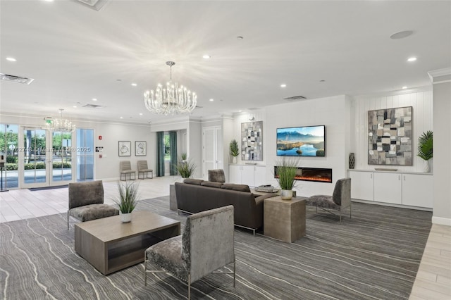 living area with visible vents, ornamental molding, wood finished floors, a lit fireplace, and an inviting chandelier