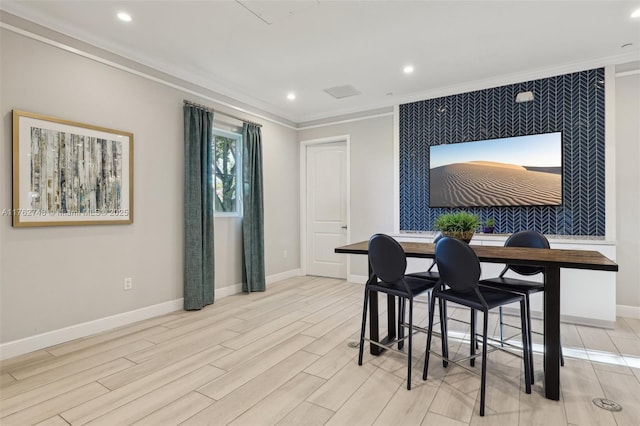 dining room featuring an accent wall, wood finish floors, baseboards, and ornamental molding