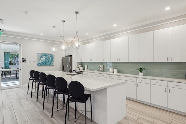 kitchen with tasteful backsplash, a sink, stainless steel fridge with ice dispenser, a breakfast bar area, and a kitchen island with sink