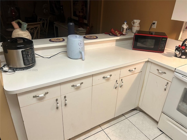 kitchen with light countertops, white cabinets, light tile patterned floors, and white range with electric stovetop