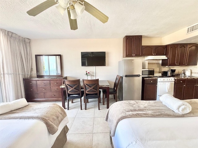 bedroom featuring visible vents, a sink, a textured ceiling, freestanding refrigerator, and light tile patterned flooring