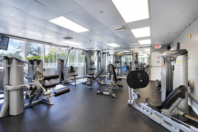 exercise room with a paneled ceiling, visible vents, and baseboards