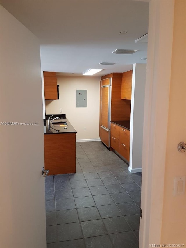 kitchen with electric panel, dark countertops, brown cabinetry, and a sink