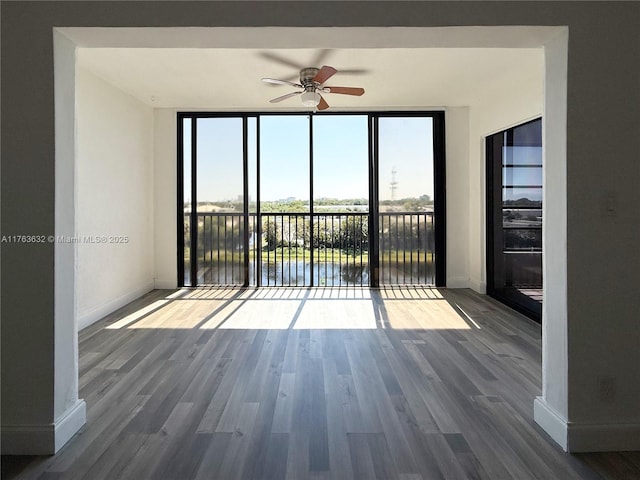 empty room featuring floor to ceiling windows, baseboards, ceiling fan, and wood finished floors